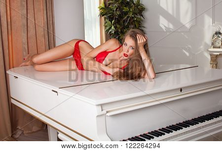 studio glamour photo of female model lying in red lingerie on piano