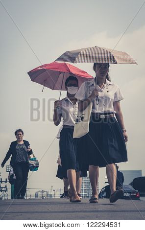 Bangkok Thailand - March 05 2014: Street portrait of two girls with umbrellas one wearing a mask. Bangkok Air pollution reaches a critical level.