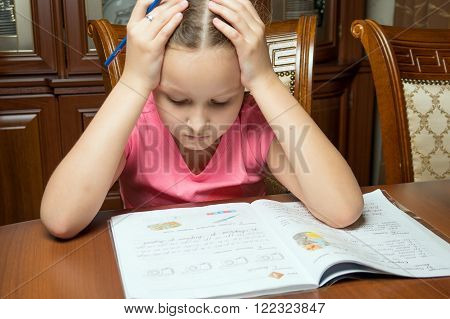 Girl doing homework. She writes in a notebook at the table.