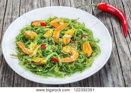delicious salad of prawns mussels seaweed chilli and sesame seasoned with extra virgin olive oil on the white dish on the old wooden table top view