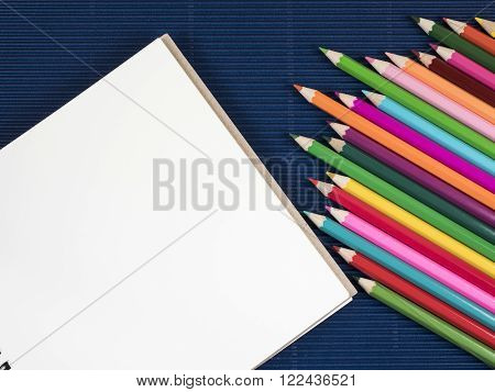 Stack of color pencil and blank notebook on blue corrugate paper background (Business object)