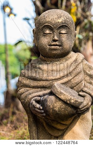 Old statue of a little monk standing and holding monk's alms-bowl