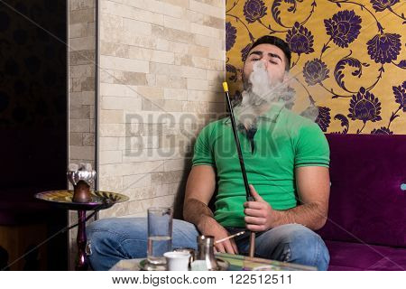 Young Man Smoking Shisha At Arabic Restaurant - Man Exhaling Smoke Inhaling From A Hookah