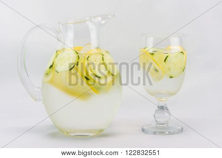 Pitcher of lemon, cucumber water and glass set against a white background.