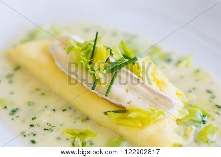 gourmet delicious omelet served with brie cheese on top in sauce with chives and celery served on white plate