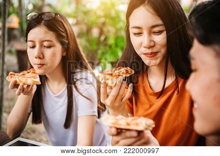 Asian students eating eating the pizza together in breaking time early next study class having fun and enjoy party, Italian food slice with cheese delicious at university outdoor.