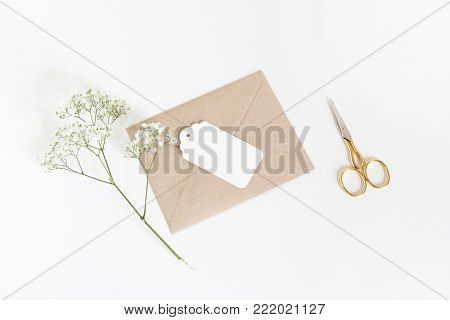 White gift tag with craft paper envelope, golden scissors and baby's breath Gypsophila flowers isolated on white table background, wedding or birthday styled stock photo, top view, flat lay composition.