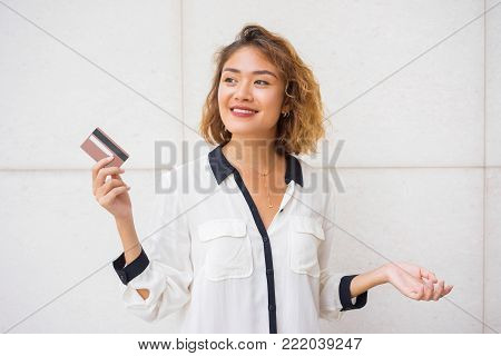 Portrait of smiling young Asian woman showing credit card. Female cardholder planning shopping. Finance and banking concept