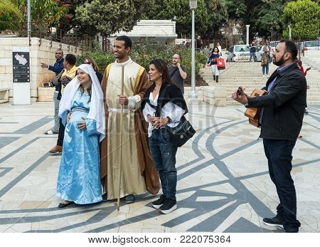 Nazareth, Israel, December 23, 2017 : A married couple - husband and pregnant wife in the clothes of Jesus' time - stand with the attendantand guitarist in front of the Basilica of the Annunciation in the old city of Nazareth in Israel