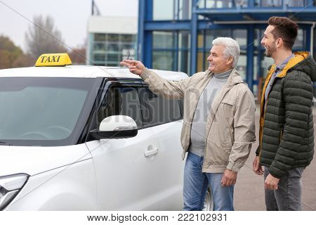 Young trainee and senior driver talking near taxi car