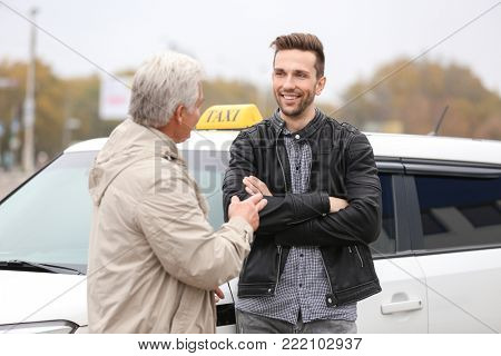 Young trainee and senior driver talking near taxi car
