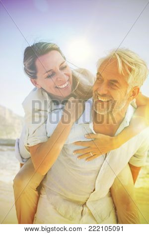 Man giving his smiling wife a piggy back at the beach on a sunny day