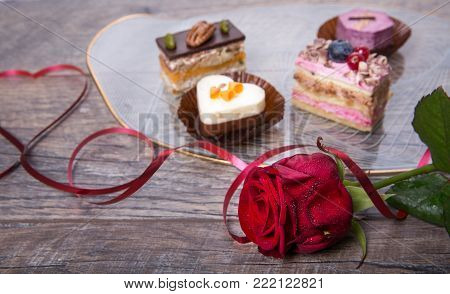 Delicious cupcake for Valentine Day. Red ribbon is lined in the shape of a heart on dark wooden table, red rose. Valentines day background, table place setting. Mother's, Women's, Wedding Day concept.