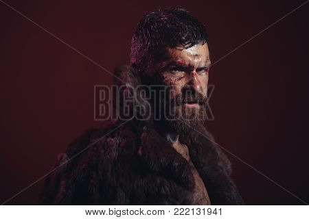 Man with beard, mustache on bloody face in fur coat on purple background. Wizard, sorcerer, warlock. Halloween, holidays celebration