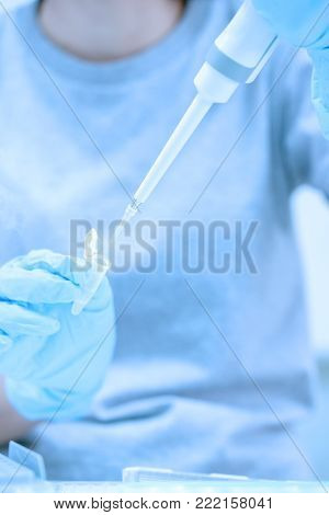 Scientist pipette dropping a sample into a test microtiter plate.
