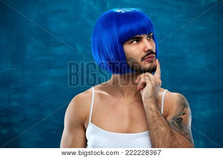 Attractive cross dressing male person wearing female clothes and blue wig posing on blue backdrop