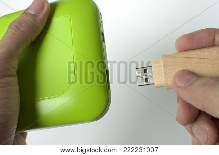 A man is inserting a wooden flashdrive in a green powerbank against white background