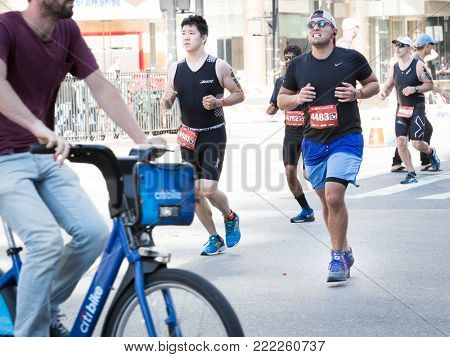 NEW YORK - JUL 16 2017: Athletes run by a bicyclist on West 72nd St during the 10k portion of the Panasonic New York City Triathlon Race, the only International Distance triathlon in NYC.