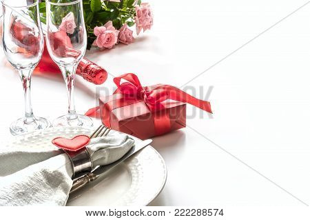 Valentines day dinner with table place setting with red gift, glass for champagne, heart ornaments with silverware on white background. Close up. Valentine's card.