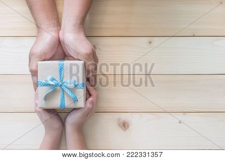 Father's day gift with daughter or son holding dad's hands giving present box with blue  ribbon on wood background to tell I love you dad and happy fathers day
