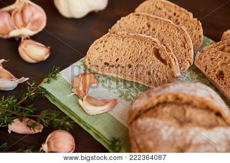 Composition of garlic and bread on a dark wooden table. Bread is cut into slices and a whole loaf is not far. Freshly baked hand-made bread on a kitchen towel.