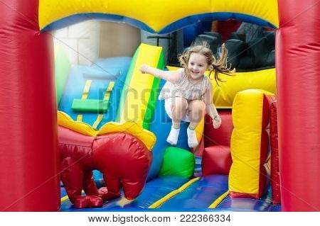 Child jumping on colorful playground trampoline. Kids jump in inflatable bounce castle on kindergarten birthday party Activity and play center for young child. Little girl playing outdoors in summer.