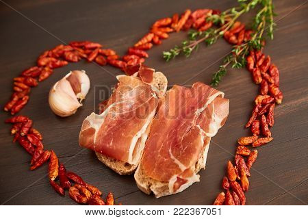 Red hot pepper is lined in the form of heart. Sandwiches made from hand-made rye bread and thin chopped fresh bacon. A branch of thyme, a clove of garlic.