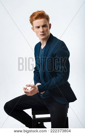 Meditation. Attractive serious red-haired young man wearing a black jacket and looking in the distance and touching his wrist
