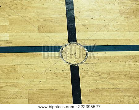 Recessed floor lid  for training equipment, Detail in floor of school gym. Black painted cross on wooden floor of sporting hall with sratched surface.