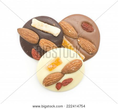 Three melted chocolate circles top view (dark, milk and white varities) with two almonds, pineapple and berry, isolated on white background