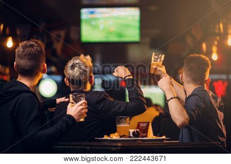 Three men watches football on TV in a sport bar