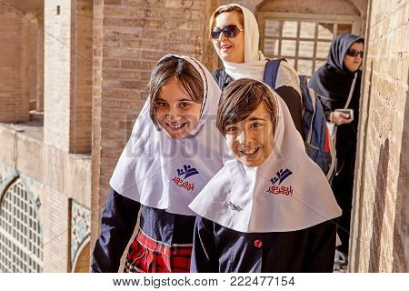 Isfahan, Iran - April 24, 2017:  Two Iranian schoolgirls, about 10 years old, dressed in school uniform with a Muslim hijab, smile while walking along the ancient Pol-e Khaju bridge, sunny day.
