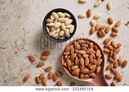 Peeled (blanched) and unblanched whole almonds. Shelled almonds on a spoon with a small black bowl of blanched almonds.