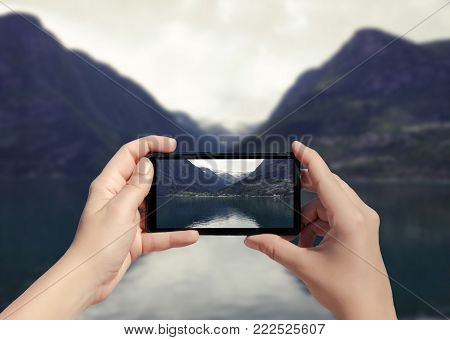 Picture of fjord in Norway on mobile phone. Female take picture of snow mountain on smart phone from ferry