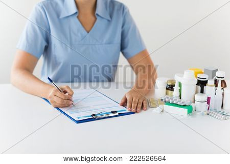 medicine, healthcare and people concept - nurse or doctor with drugs and clipboard writing prescription or medical report at hospital