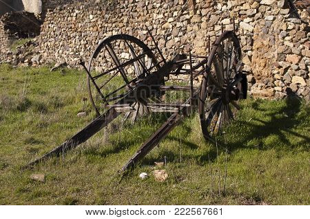 Remains of a rusty old carriage in Spain with stone wall as background