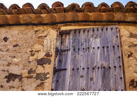 Old wooden window with rusty hinges on an old stone house facade.