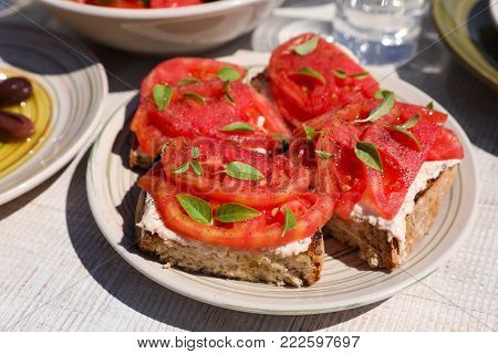 Sandwiches with feta cheese, fresh tomatoes, basil leaves as an appertizer in greek tavern. Horizontal. Daylight. Close-up.