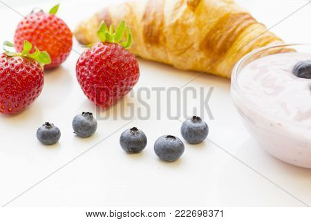 Healthy Breakfast Concept with a fresh buttery croissant, a bowl of fresh homemade youghurt with blueberries and strawberries on white, close up, copy space