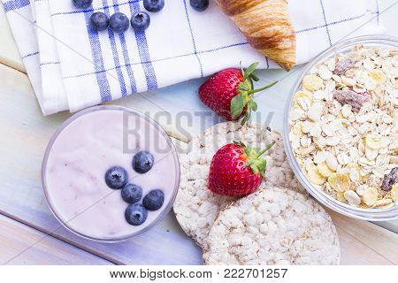 Romantic French or Rural Breakfast with croissant, wheat breadcrisps, muesli, with fresh strawberries and blueberries and youghurt. Napkin and wood as a background, top view
