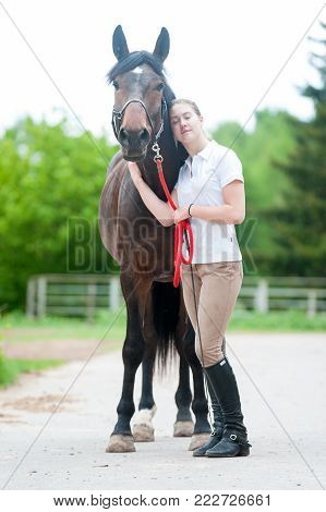 Young teenage girl enjoying of hugging her favorite chestnut horse with closed eyes. Colored outdoors vertical summertime image.