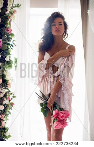 girl in lingerie standing by the bed with flowers