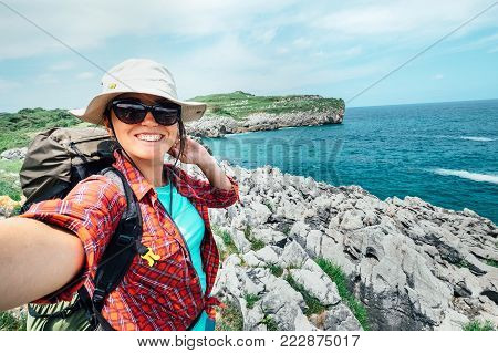 Happy woman backpacker traveler take a selfie photo on amazing ocean coast. Asturias. Spain