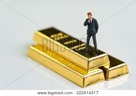 Miniature figure businessman standing and thinking on shiny gold bullions ingot as finance fund manager, investment and wealth concept.
