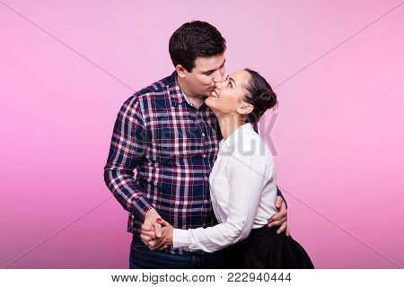 Happy husband and wife in studio on pink background looking at eatch other