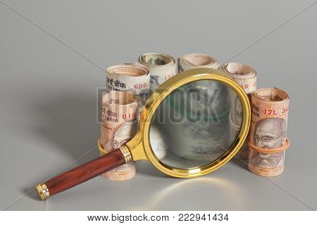 Rolls of Indian Currency Rupee Notes with magnifying glass on gray