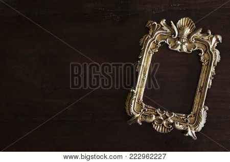 antiq golden photo frame in Rococo style, on dark rustic wooden background