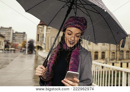 Beautiful young woman with umbrella using mobile phone in the city