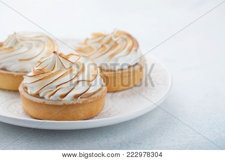 Lemon tartlets with meringue on vintage white plate on the stone table. Tasty treat on a light blue background. With copy space.
