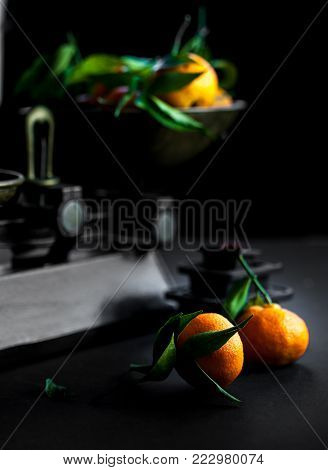 A bunch of fresh juicy clementines with green leaves in a scalepan and on a black table